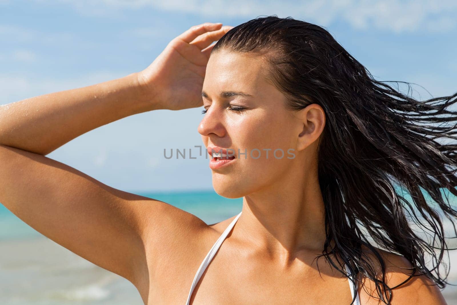 Young attractive woman with dark hair on the beach looks into the distance in the sunshine