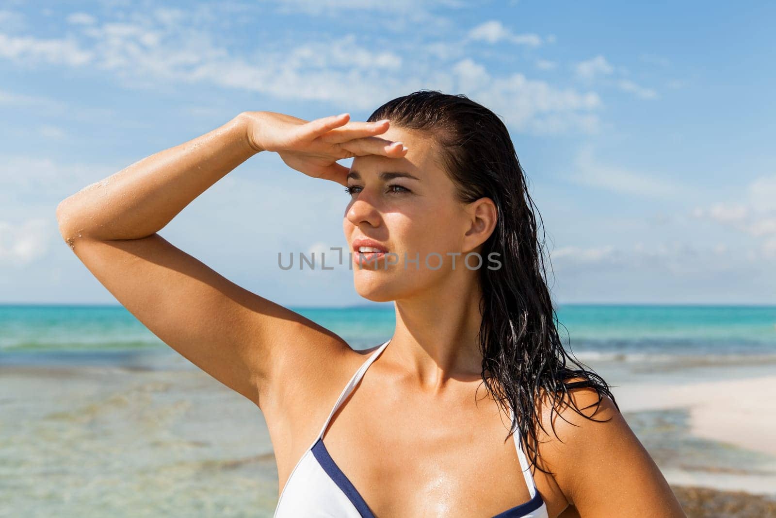 Young attractive woman with dark hair on the beach looks into the distance in the sunshine