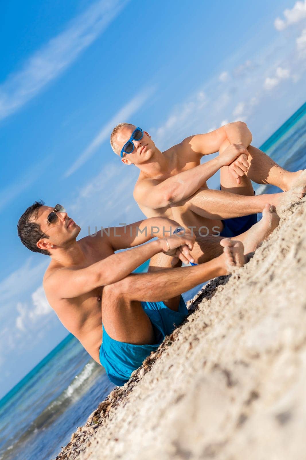 Two young men friends relax in the sand while on holiday on the beach in summer