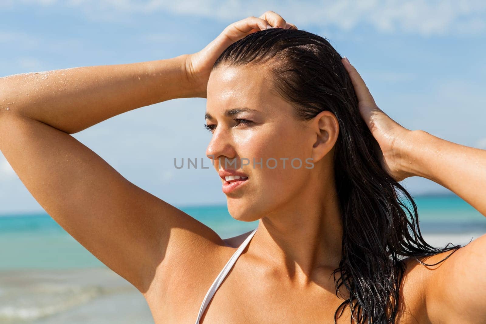 Young attractive woman with dark hair on the beach looks into the distance in the sunshine