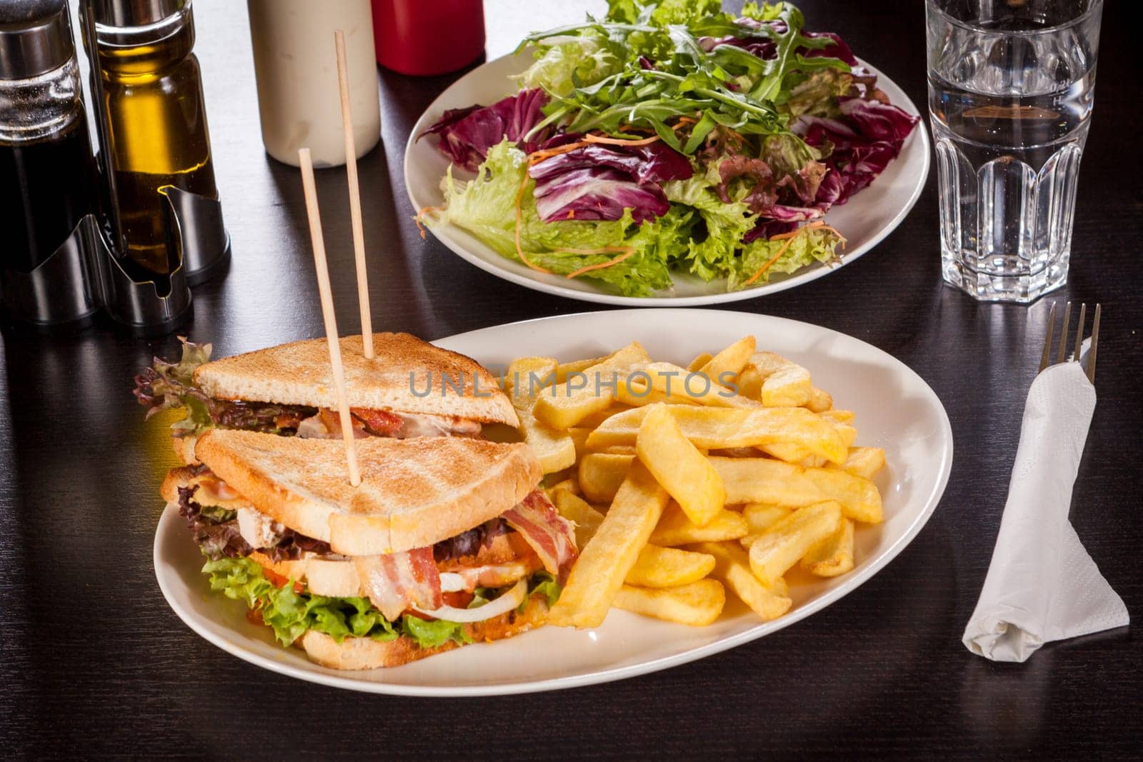 Club sandwich on toasted white bread with bacon and fries fried fries on a plate