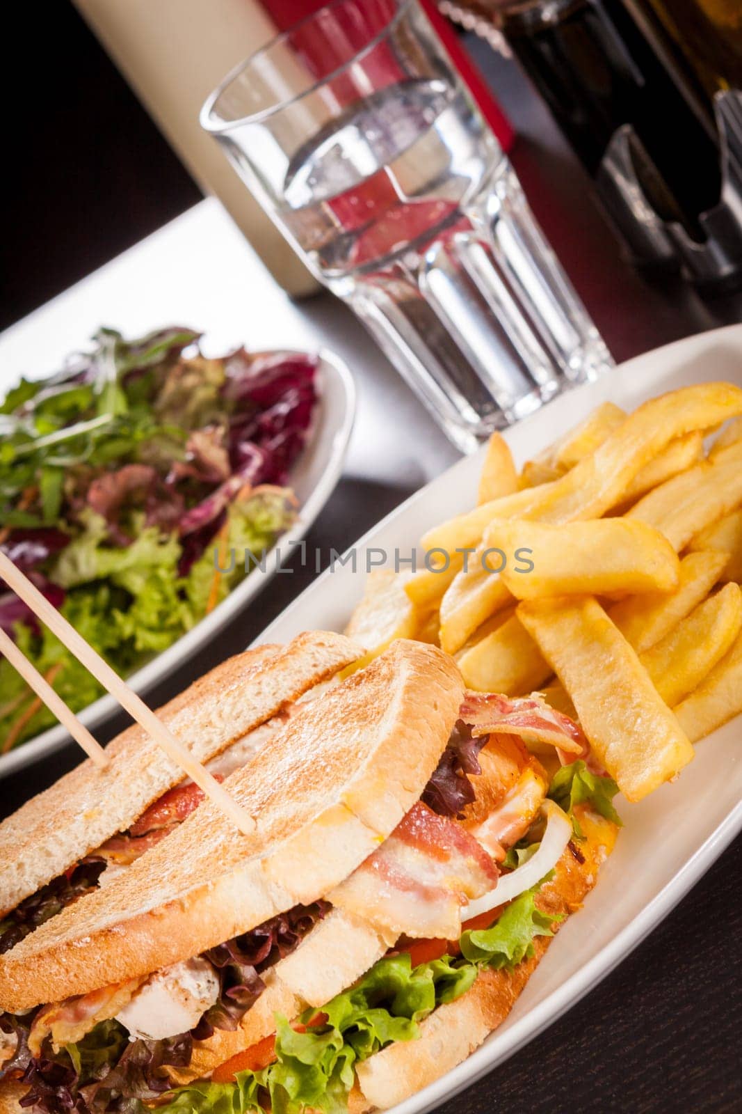 Club sandwich on toasted white bread with bacon and fries fried fries on a plate