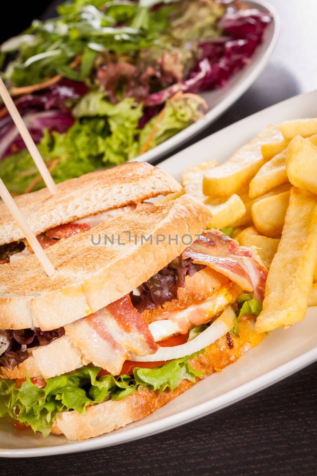 Club sandwich on toasted white bread with bacon and fries fried fries on a plate