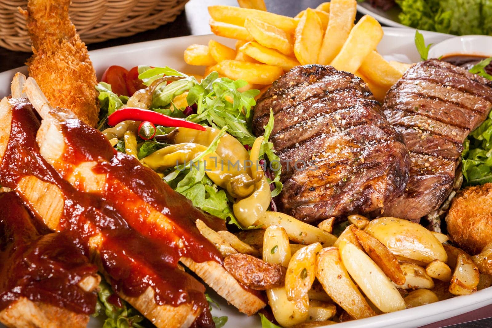 Huge barbecue plate with mixed meat and steaks on salad