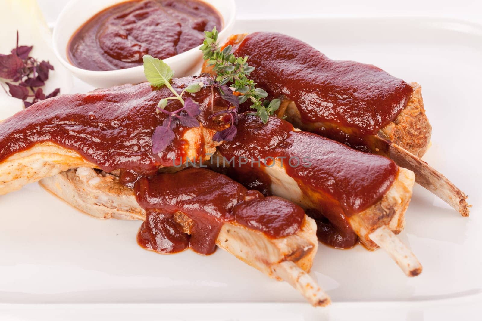 Grilled pork ribs Spareribs with barbecue sauce marinade and herb salad on a plate isolated against a white background