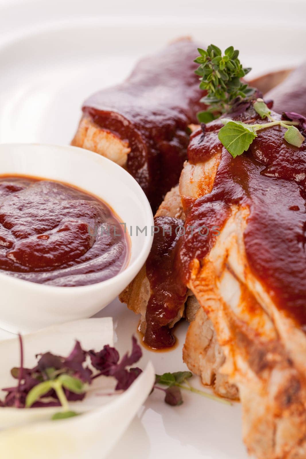 Grilled pork ribs Spareribs with barbecue sauce marinade and herb salad on a plate isolated against a white background