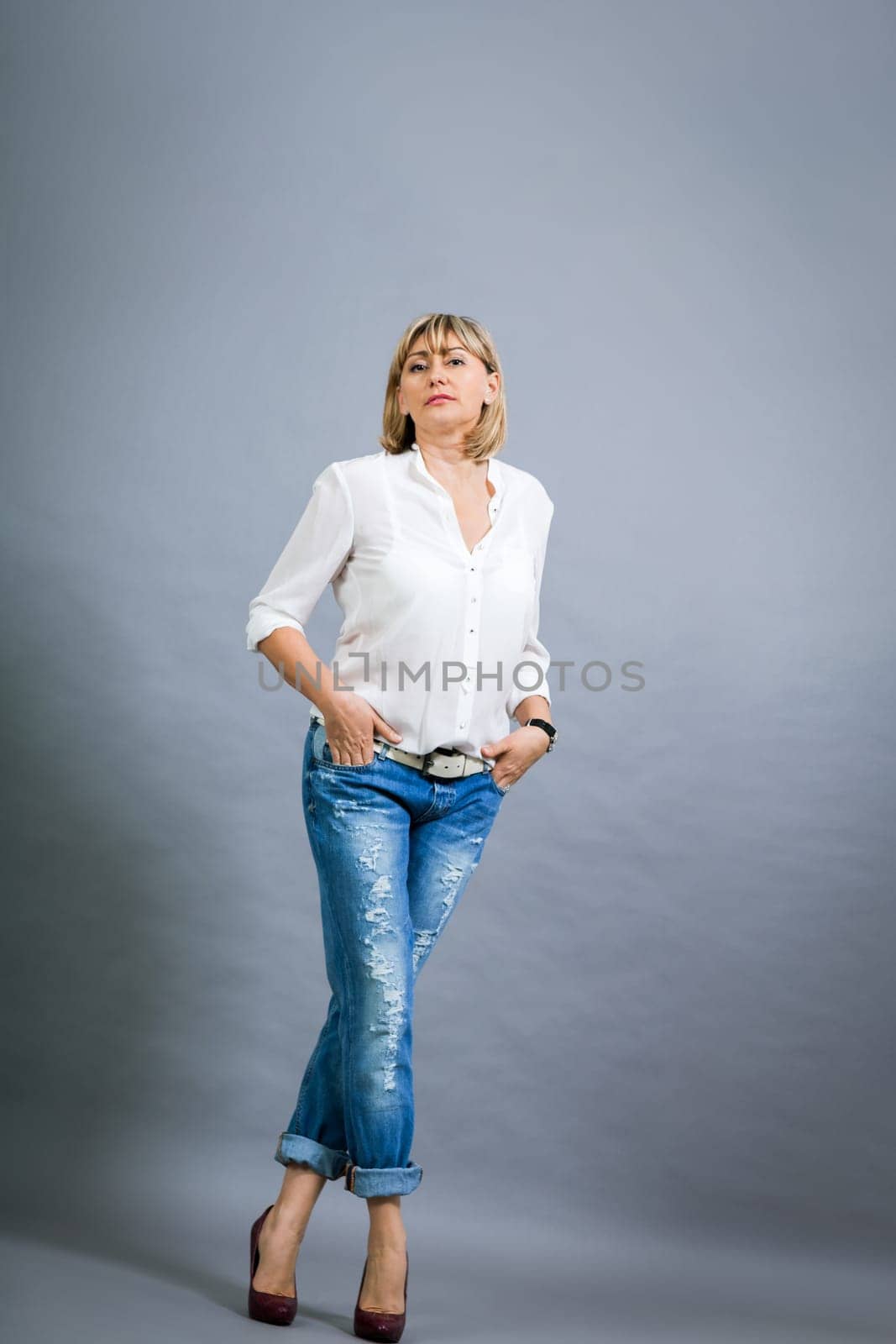 adult blonde attractive woman with blue jeans and white blouse against grey background fashion trendy