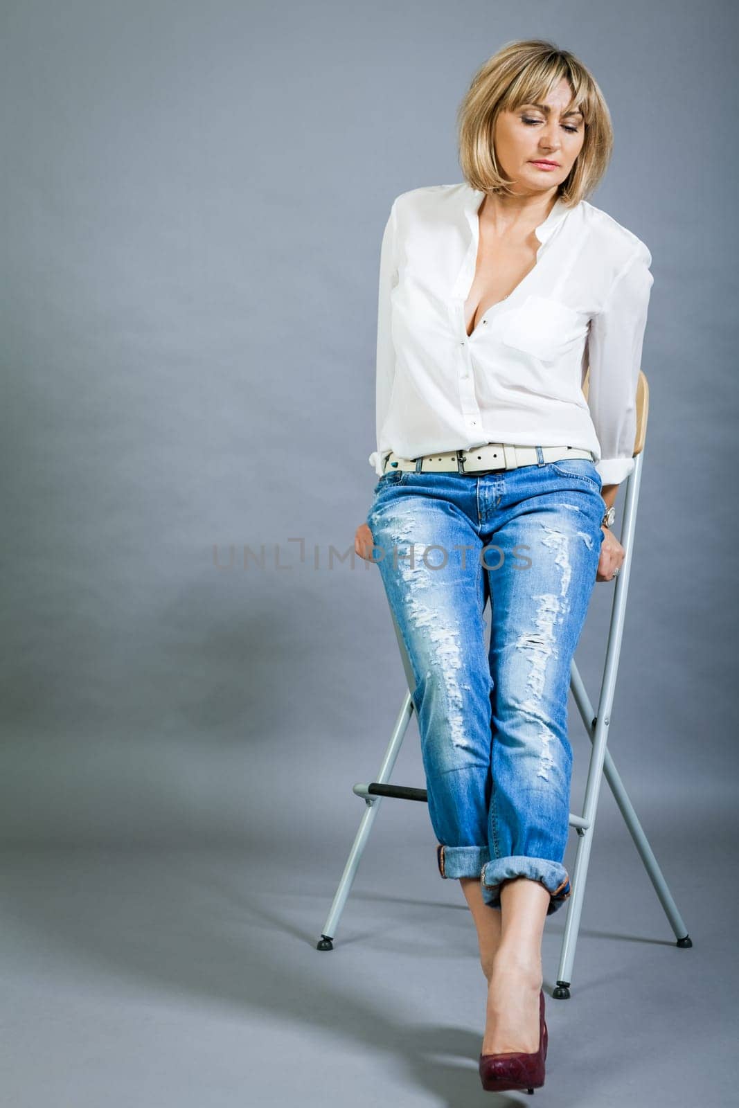 adult blonde attractive woman with blue jeans and white blouse against grey background fashion trendy