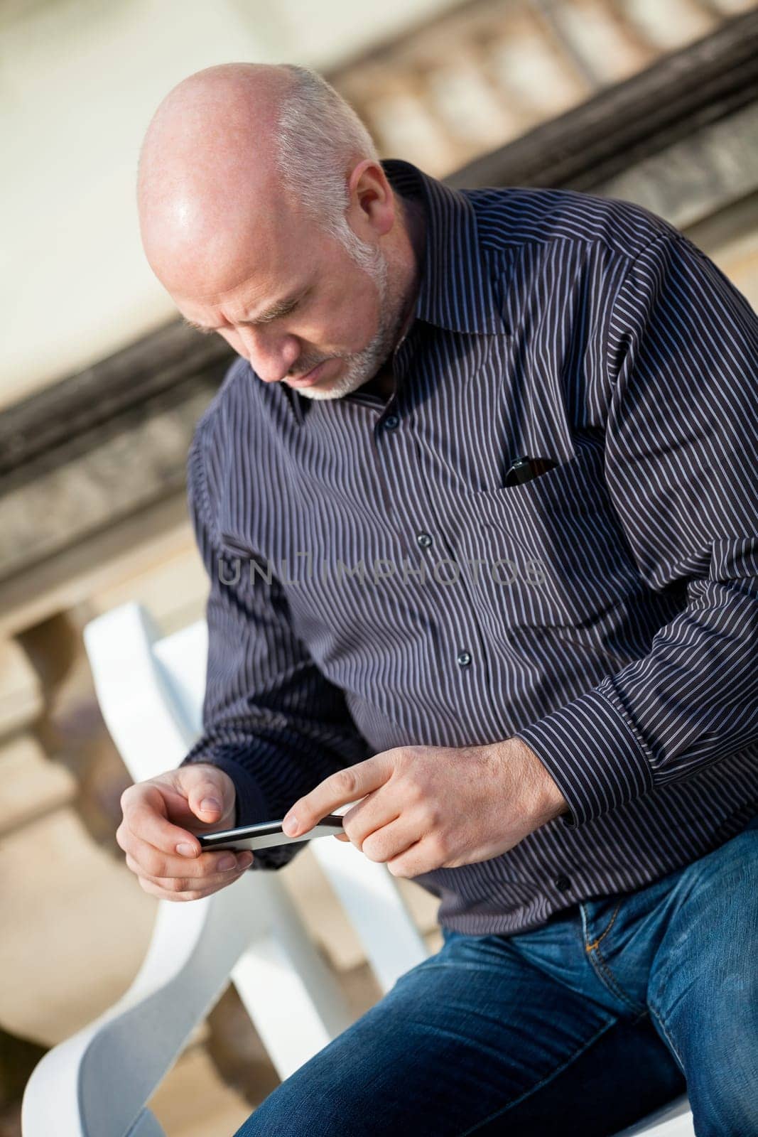 Attractive older man senior with mobile phone smartphone on a bench in the park in summer