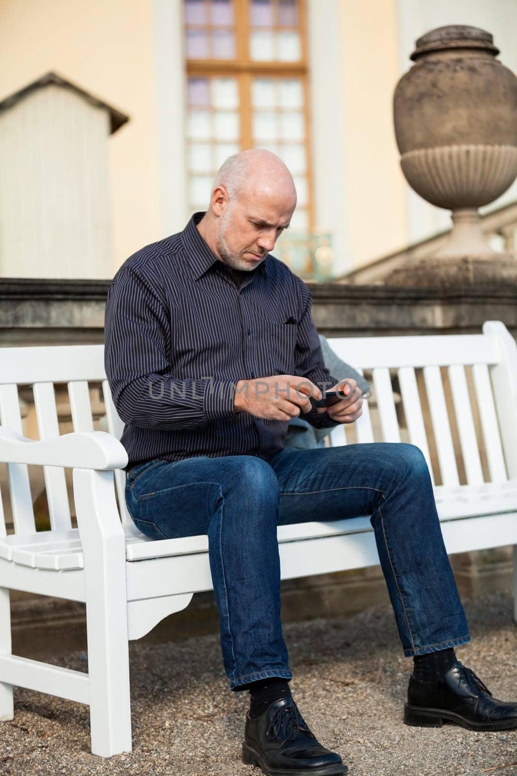 Attractive older man senior with mobile phone smartphone on a bench in the park in summer