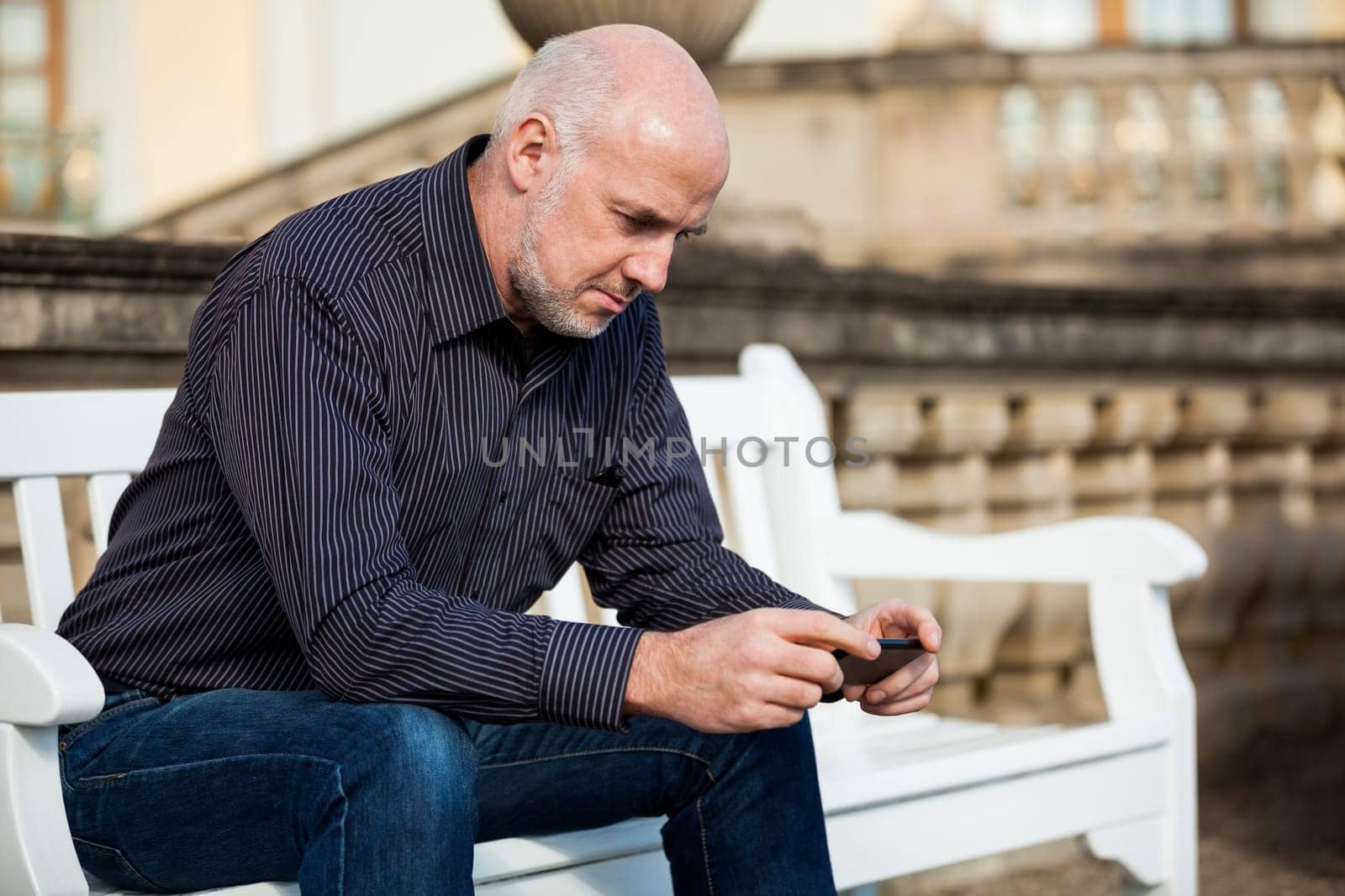 Attractive older man senior with mobile phone smartphone on a bench in the park in summer