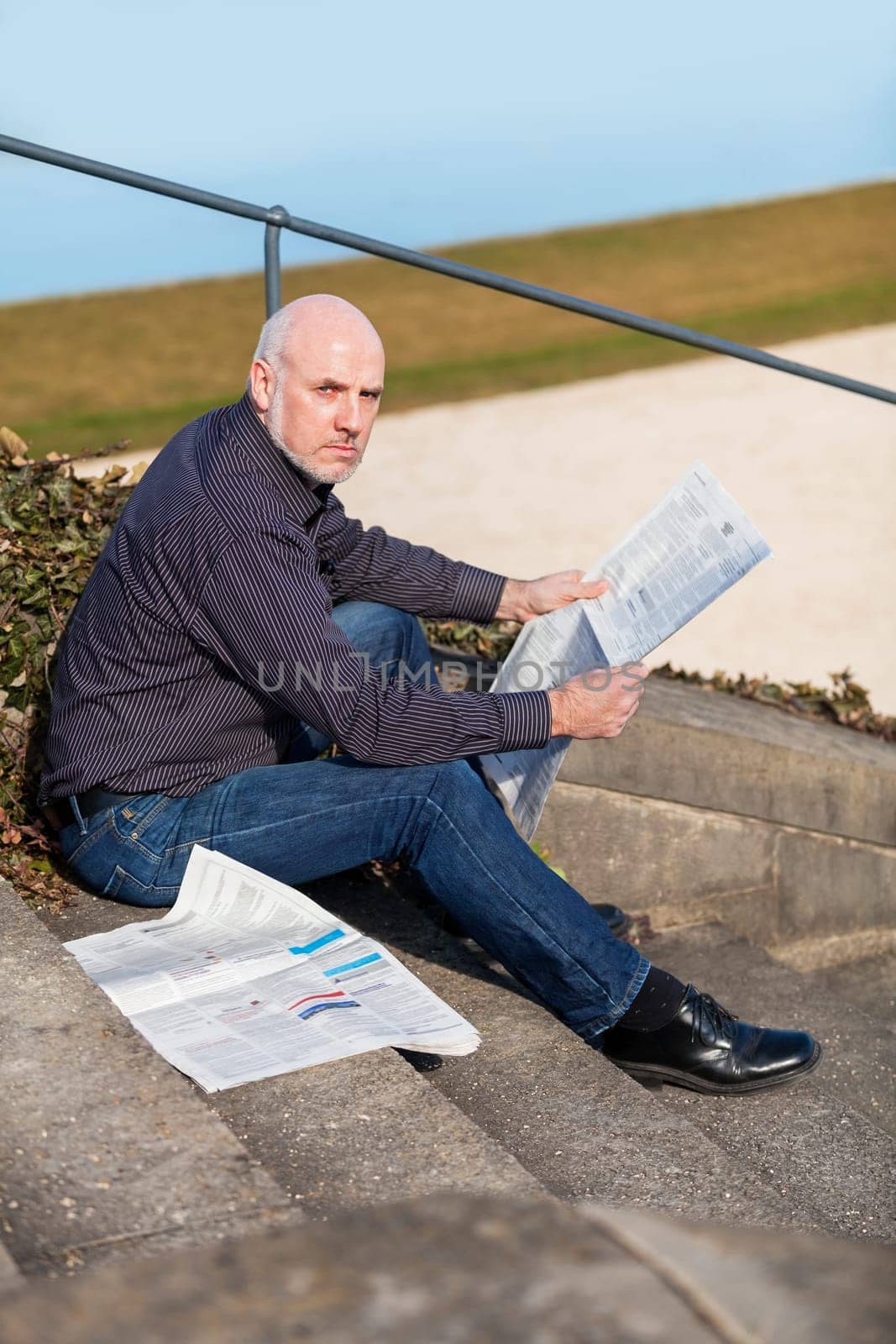 Middle-aged man,senior sitting with a newspaper on a staircase in spring outdoors
