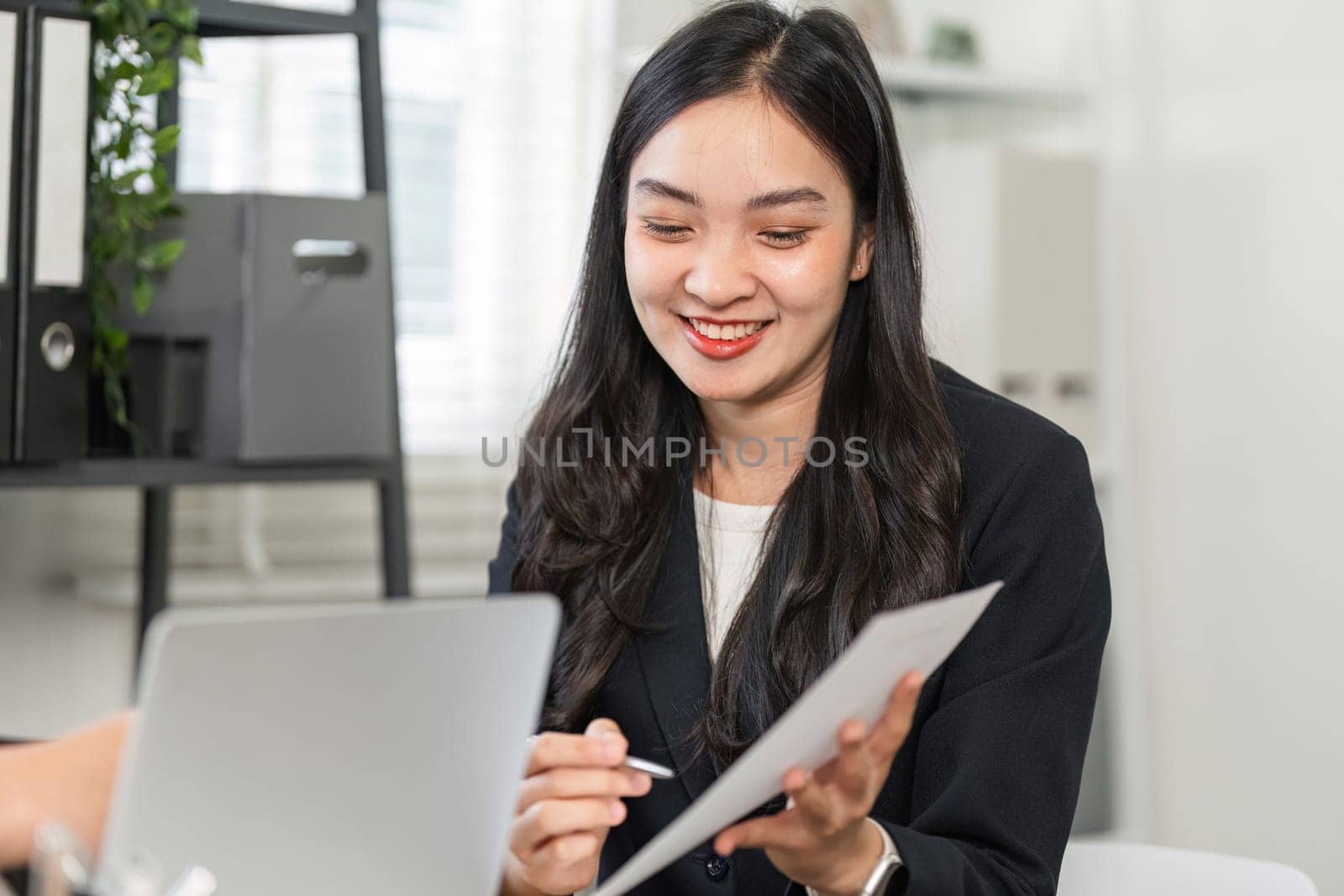 A confident businesswoman smiles while reviewing documents and collaborating with a colleague in a contemporary office environment.