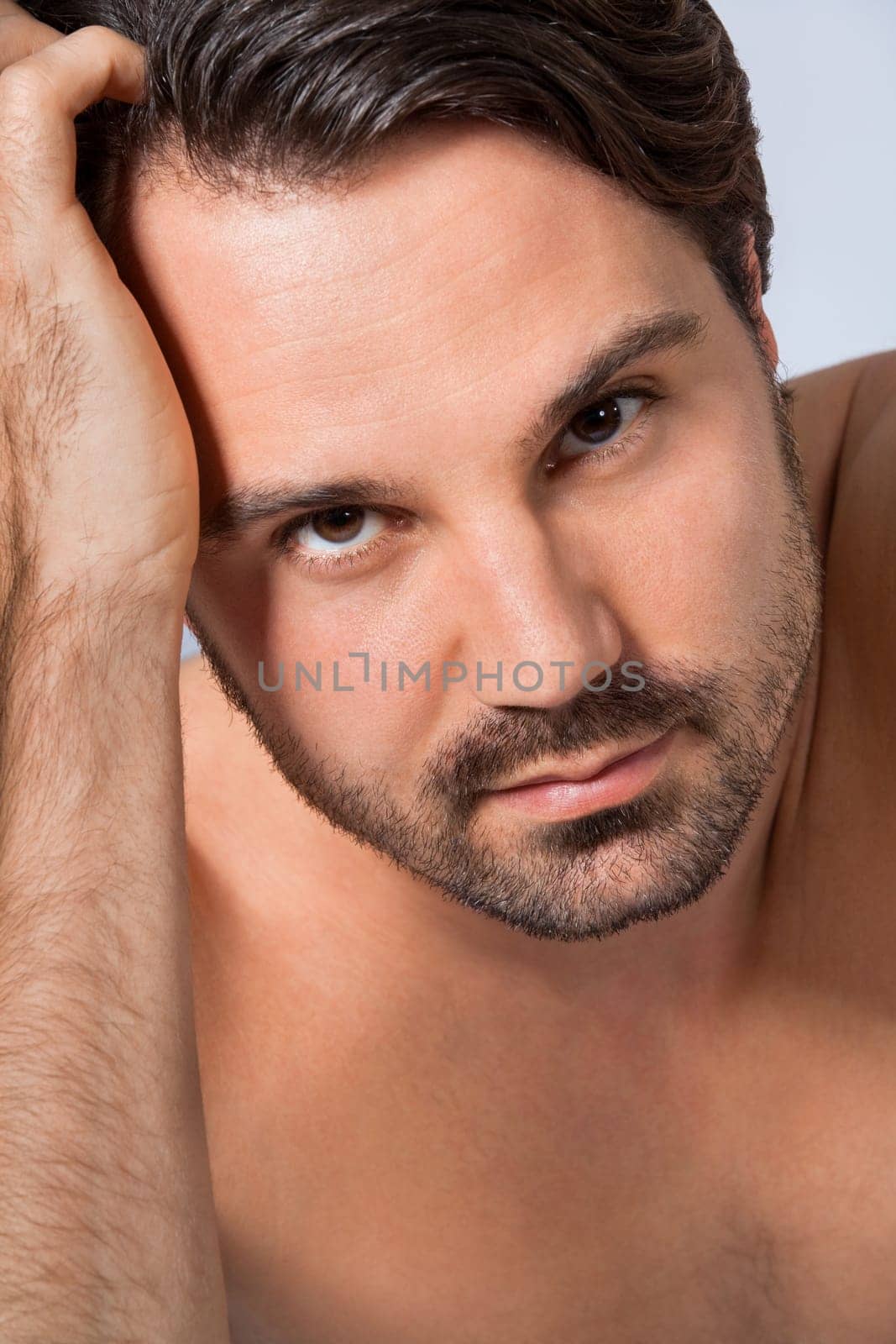 Young naked man with dark hair and beard as a portrait against a grey background