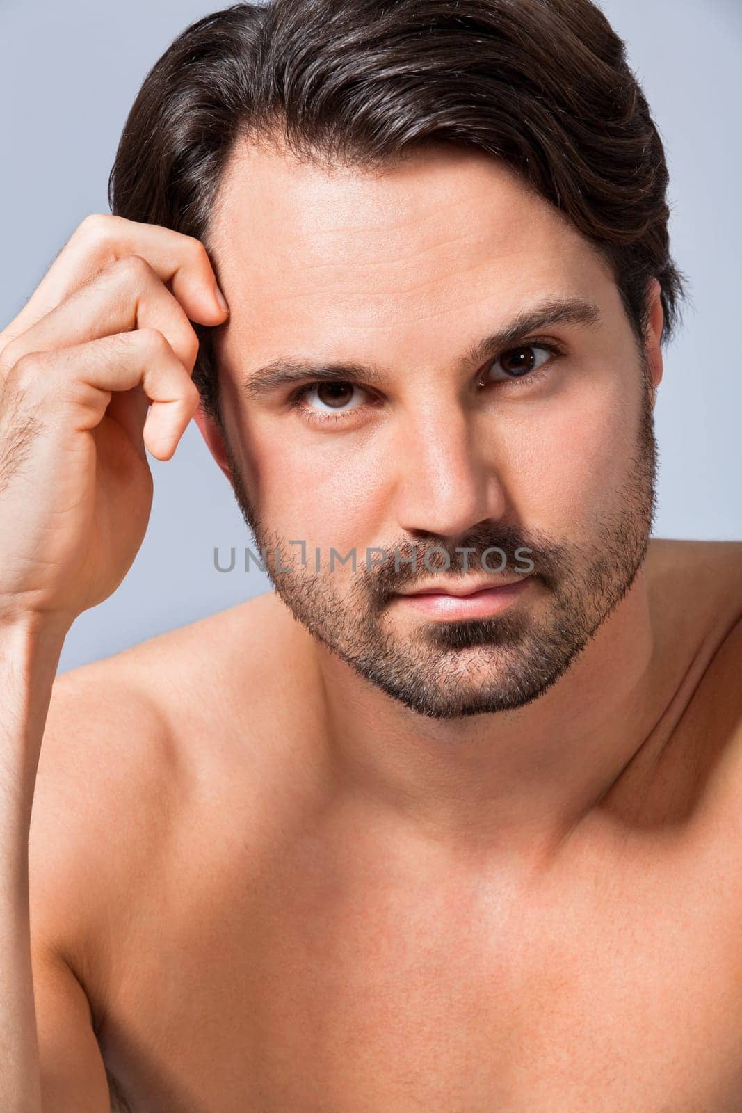 Young naked man with dark hair and beard as a portrait against a grey background
