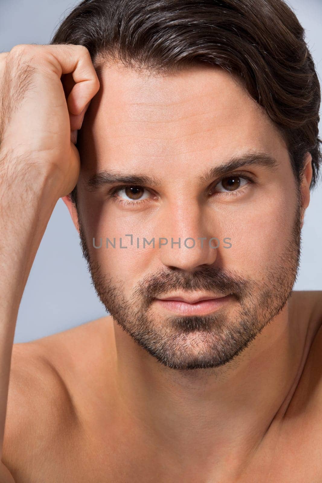 Young naked man with dark hair and beard as a portrait against a grey background
