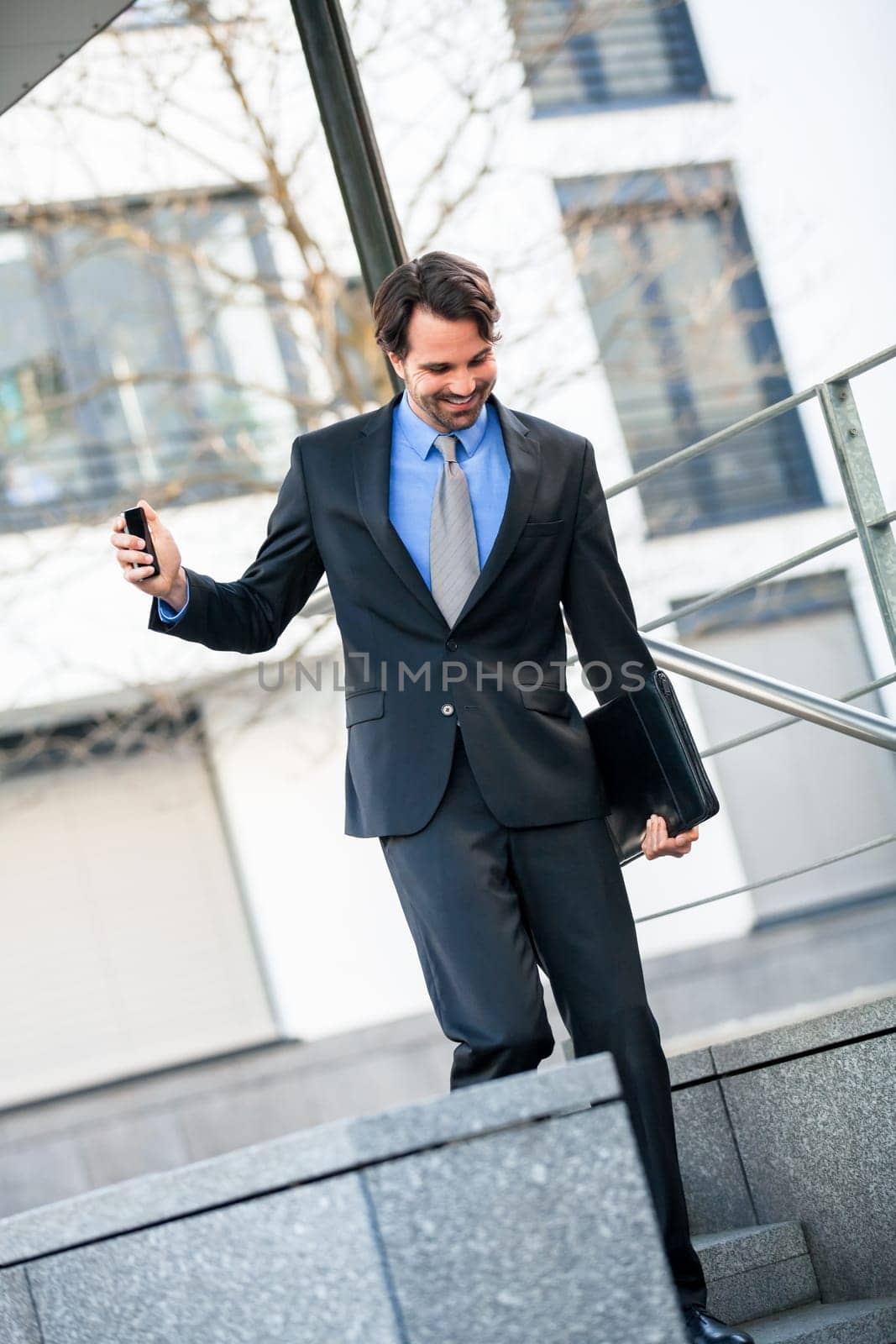 Cheerful successful businessman with dark suit and dark hair joyfully in front of a commercial building