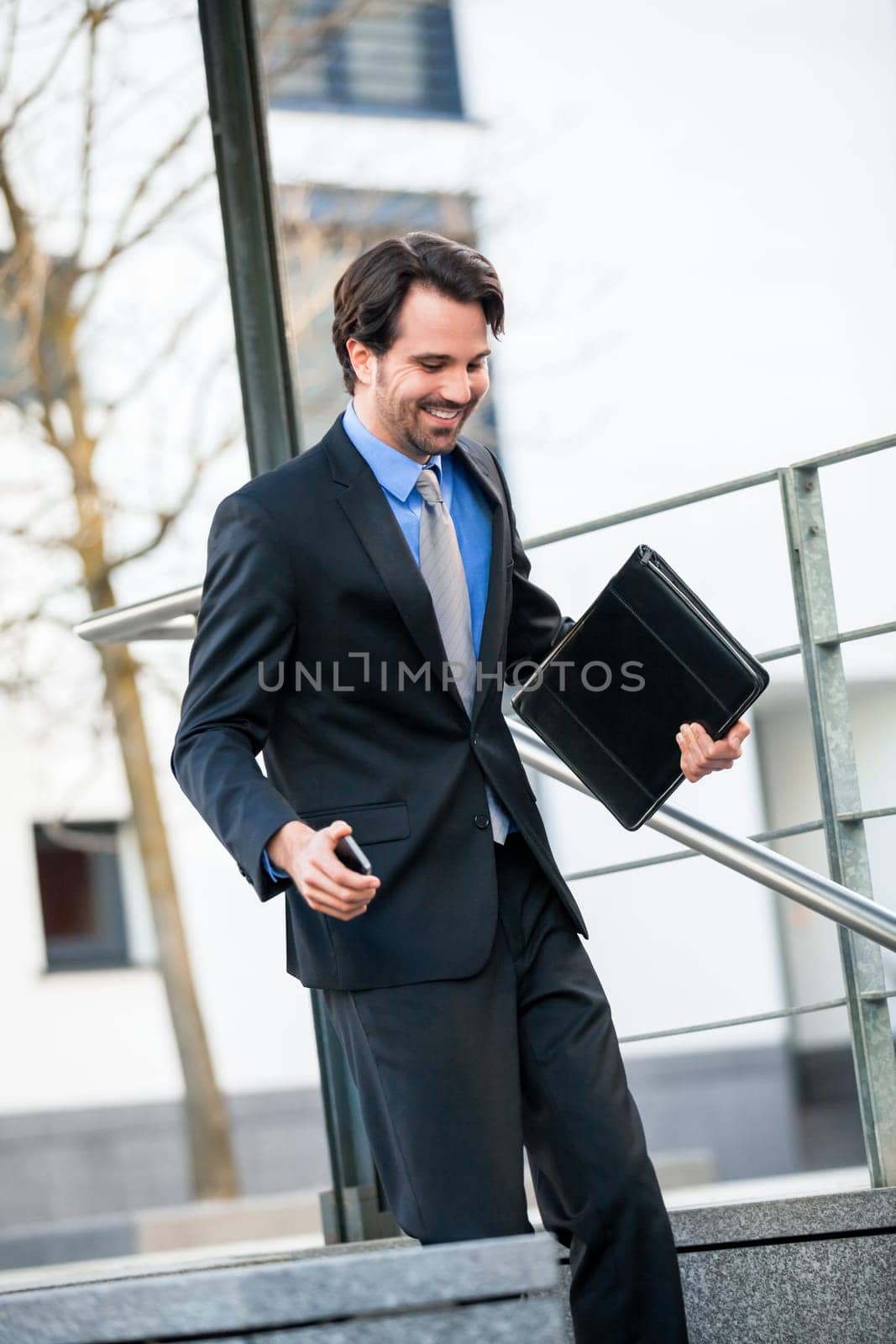 Cheerful successful businessman with dark suit and dark hair joyfully in front of a commercial building