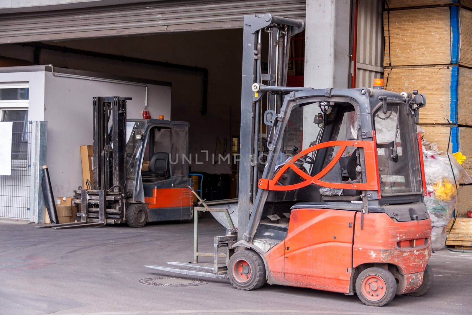 Small orange forklift in front of a warehouse with freight traffic and goods in the background