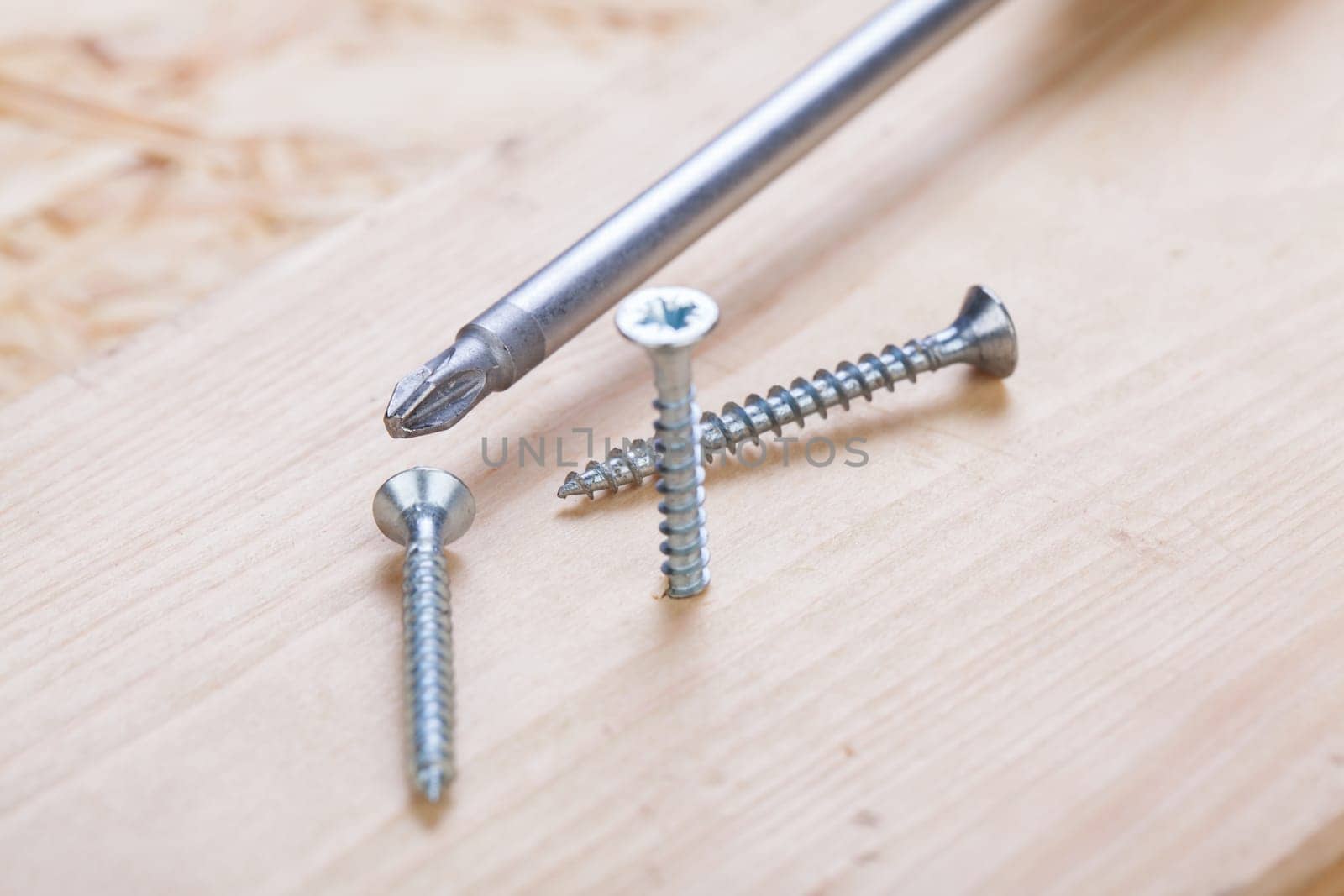 Close-up of a cross screwdriver with screws in wood while DIY in a workshop