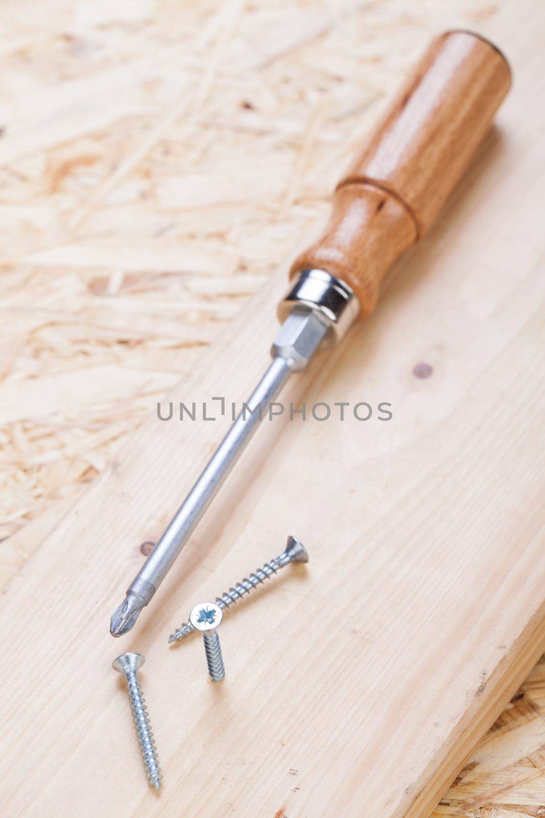 Close-up of a cross screwdriver with screws in wood while DIY in a workshop