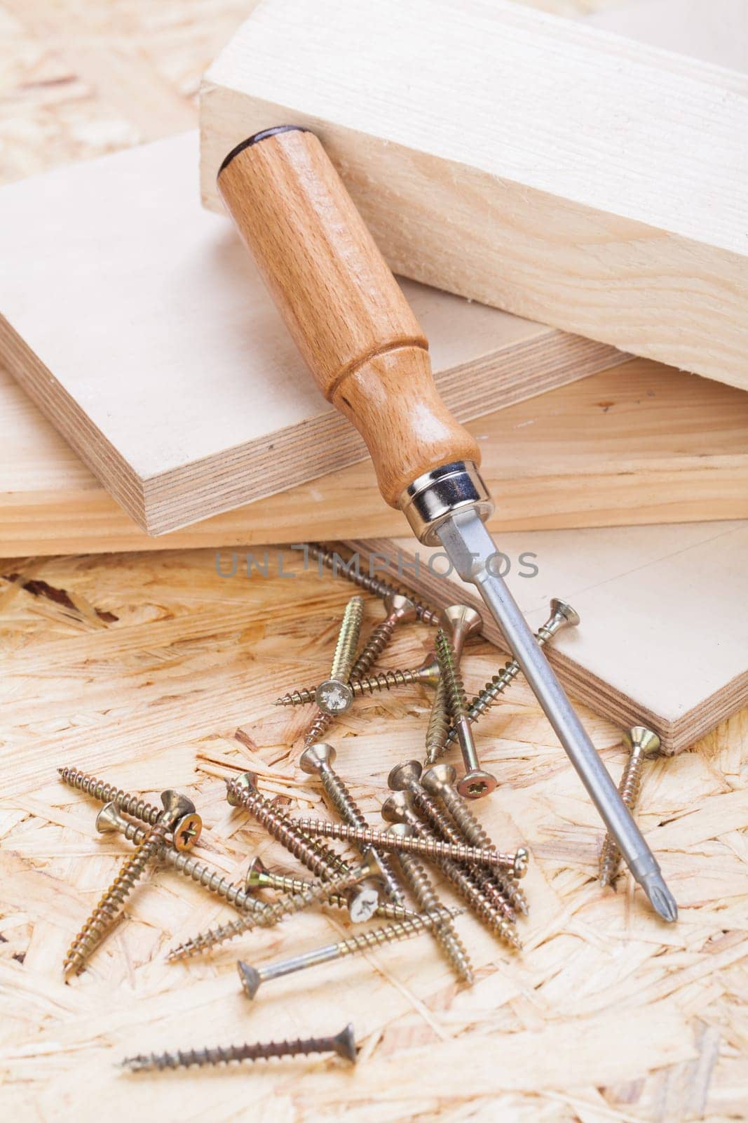 Close-up of a cross screwdriver with screws in wood while DIY in a workshop