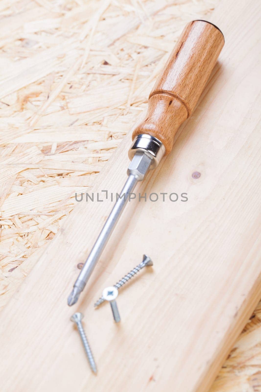 Close-up of a cross screwdriver with screws in wood while DIY in a workshop