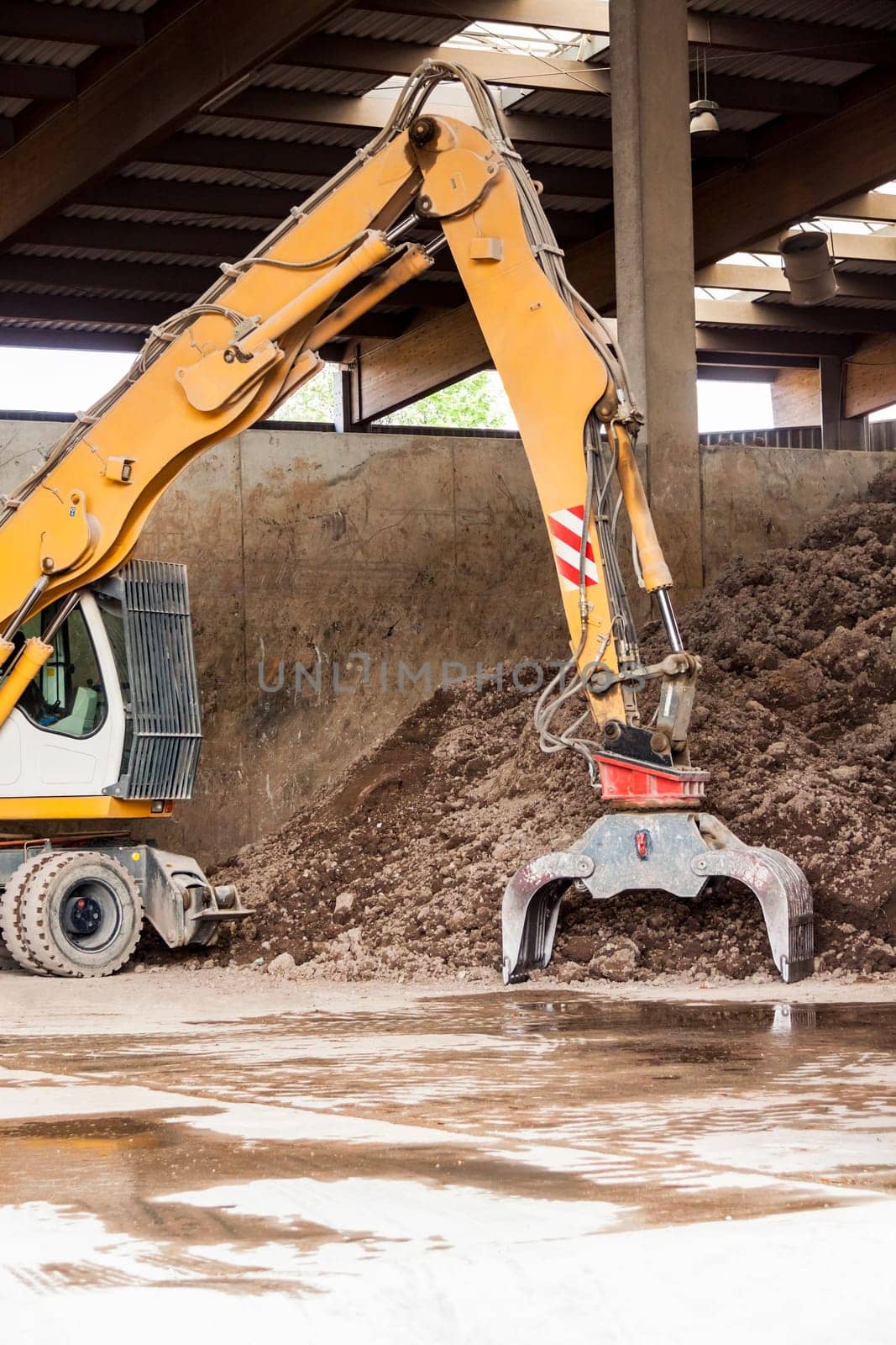 Excavator with gripper arm in front of a large pile of brown earth in the construction industry