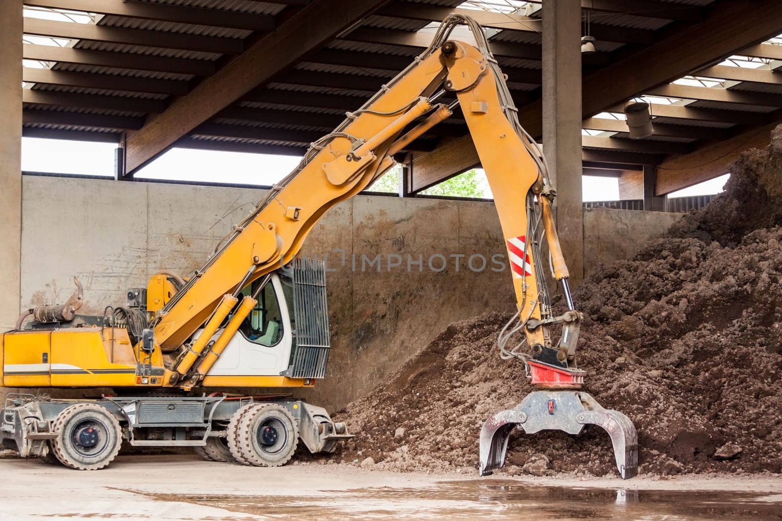 Excavator with gripper arm in front of a large pile of brown earth in the construction industry