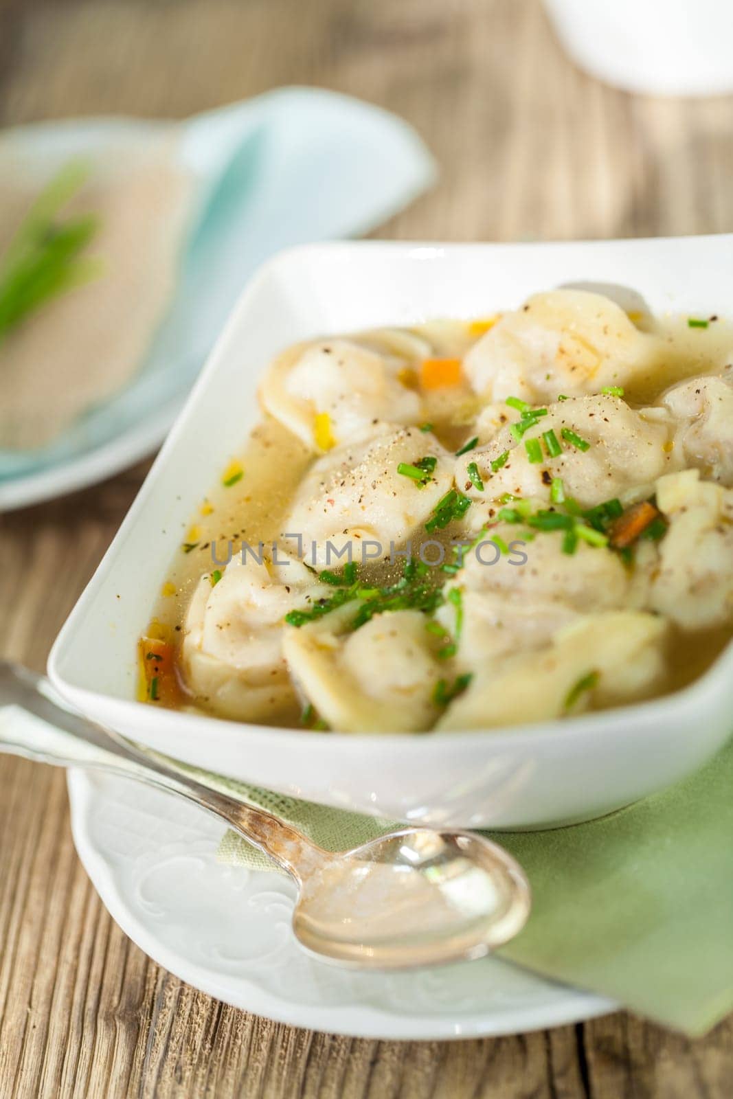 Bowl with Russian Pelmeni Italian tortellini with broth and parsley close-up on a wooden table