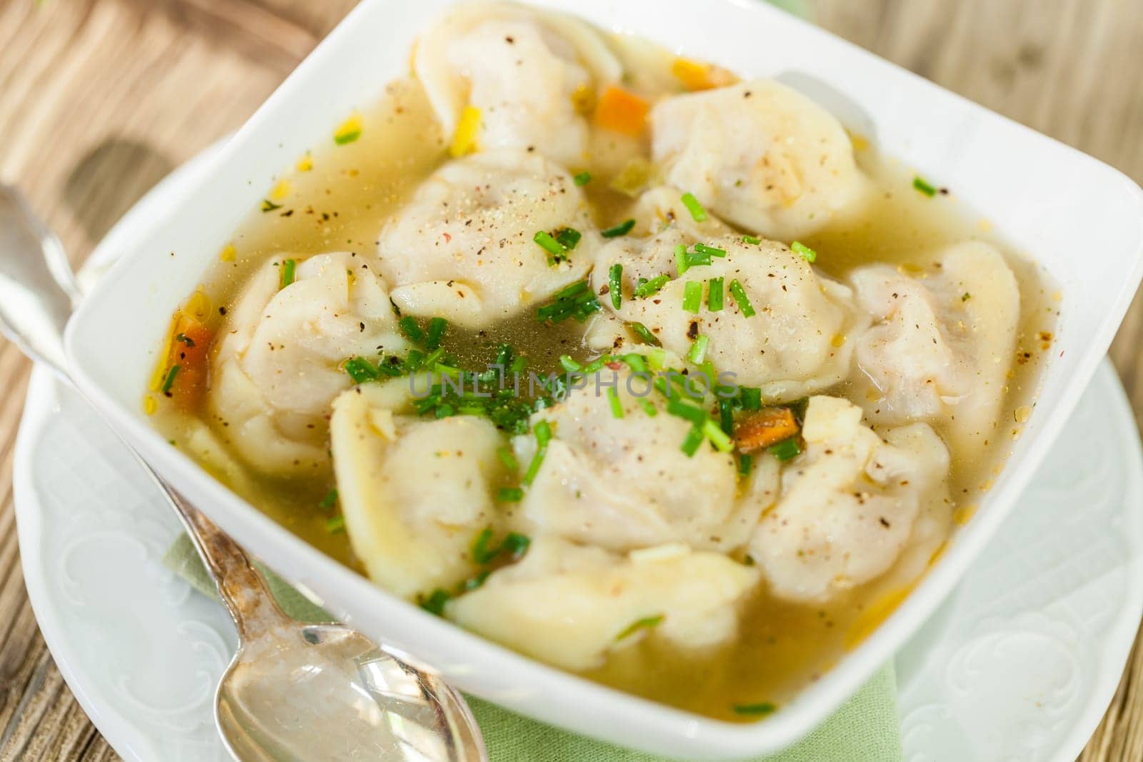Bowl with Russian Pelmeni Italian tortellini with broth and parsley close-up on a wooden table