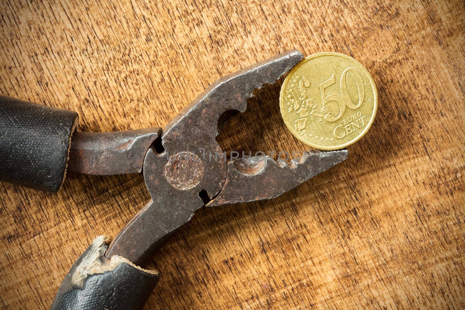 Euro cent and pliers on the wooden background. Money concept.