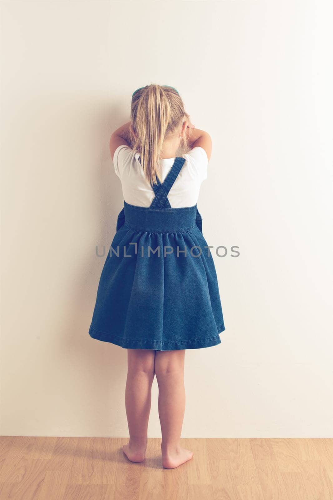 portrait of sad little girl standing near wall. studio shot