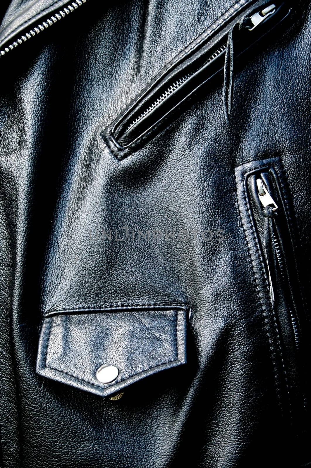 High contrast close up of black leather biker jacket showing zippered pockets and coin pocket with snap button and portion of belt in sunshine.