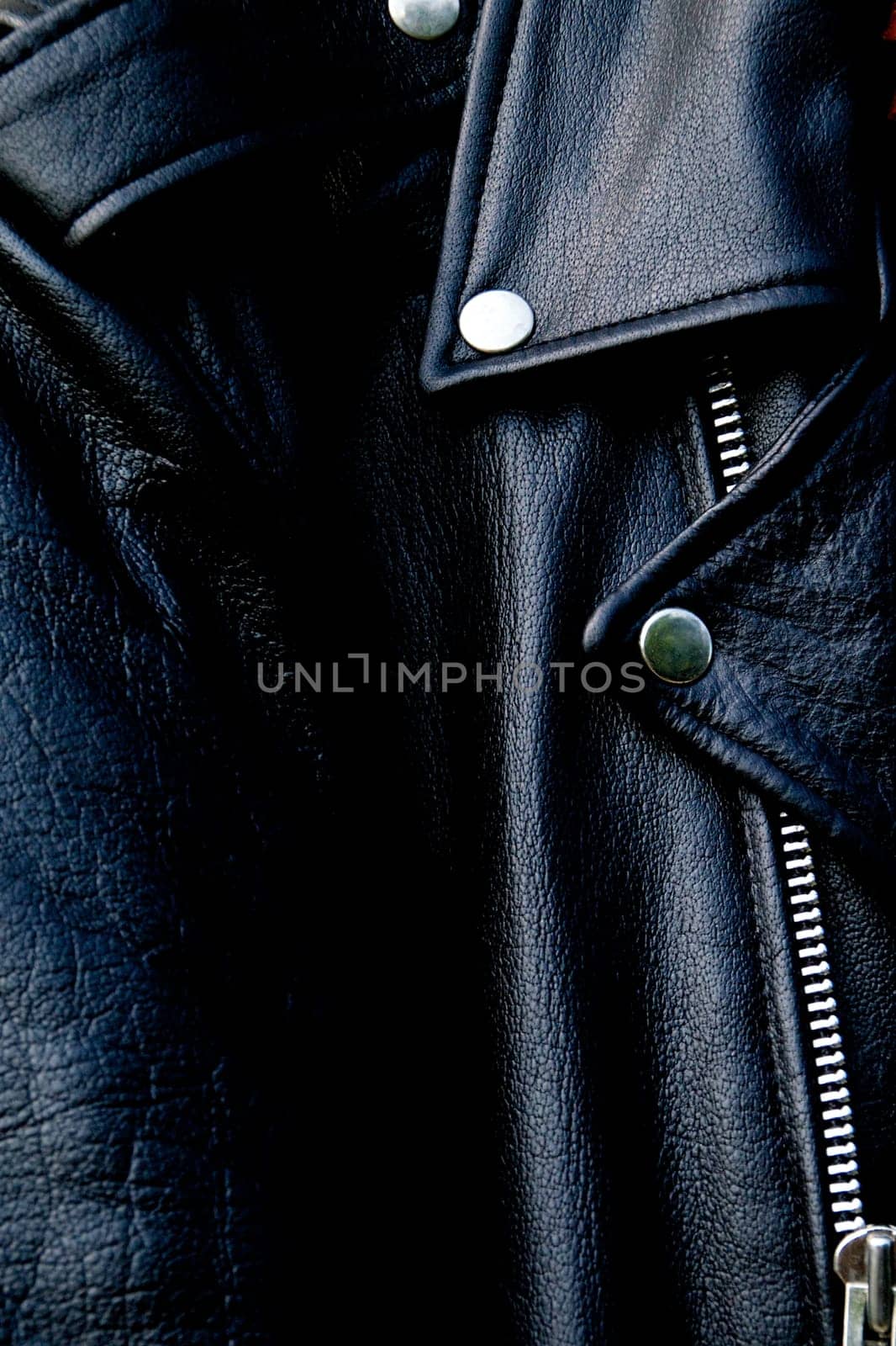 High contrast close up of black leather biker jacket showing zipper, shoulder and snap collar and lapel in sunshine.