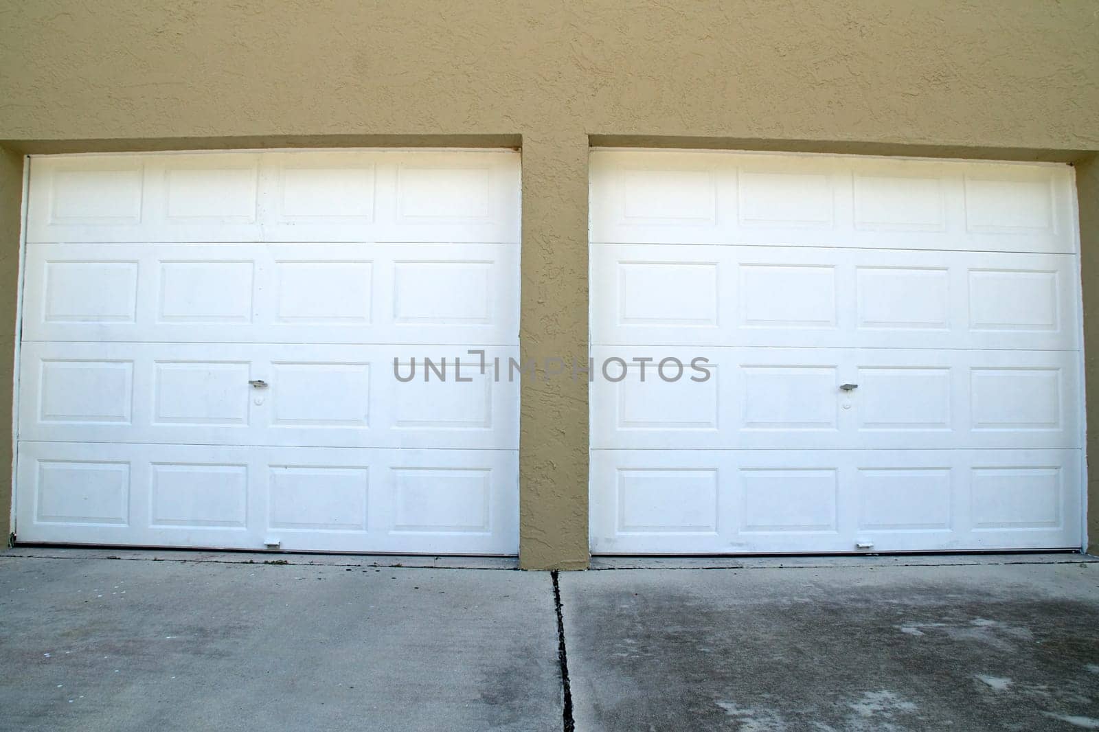 Wide angle view of two white closed garage doors at top of cement driveway