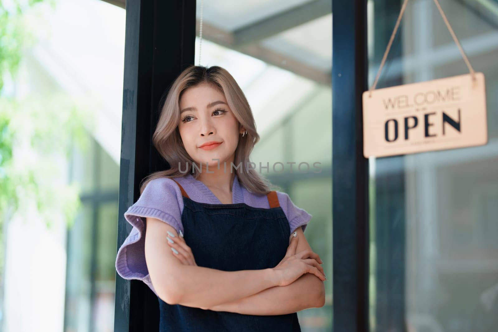open a small business Portrait of happy Asian woman wearing apron holding welcome we are open sign at front of cafe