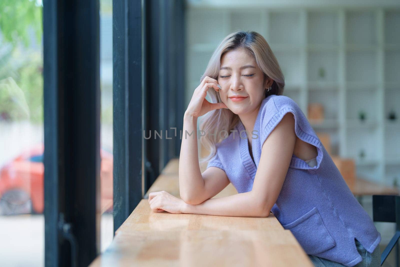 Asian young woman making notes in paper notebook sitting on cozy sofa on background of window. Pretty female writing notes in diary or making to do list relaxing at home