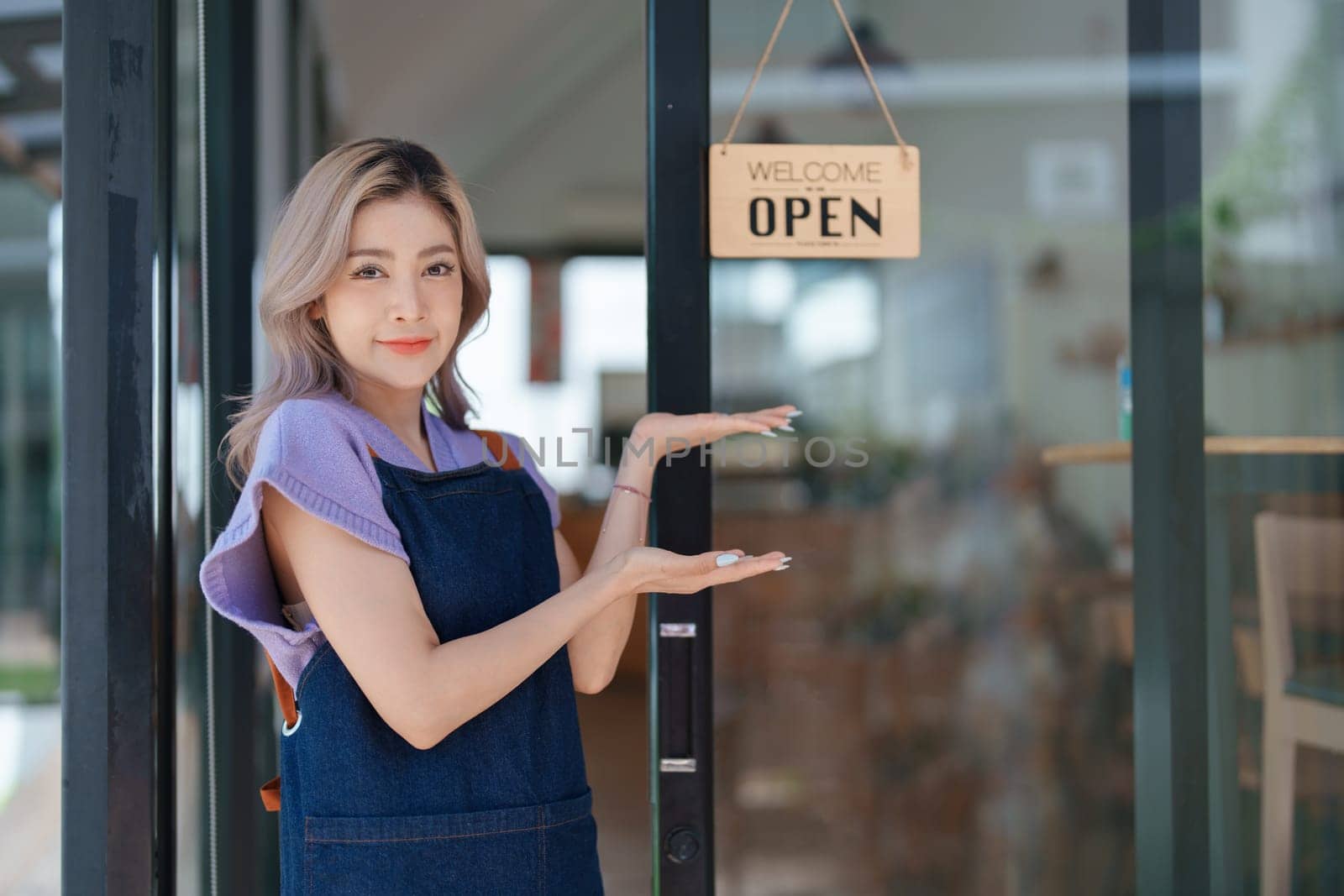 open a small business Portrait of happy Asian woman wearing apron holding welcome we are open sign at front of cafe