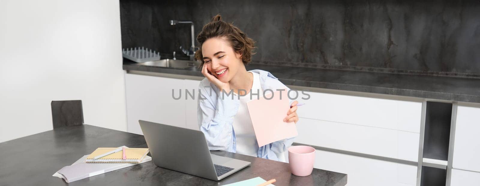 Portrait of young professional woman, works from home, looks at laptop, studies online, connects to a webinar, work remote meeting via computer, video chats with tutor from courses website by Benzoix