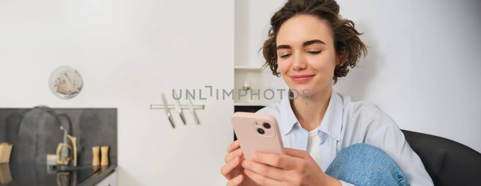 Smiling brunette girl sitting with smartphone at home, orders takeaway from mobile phone app, using online shopping application.