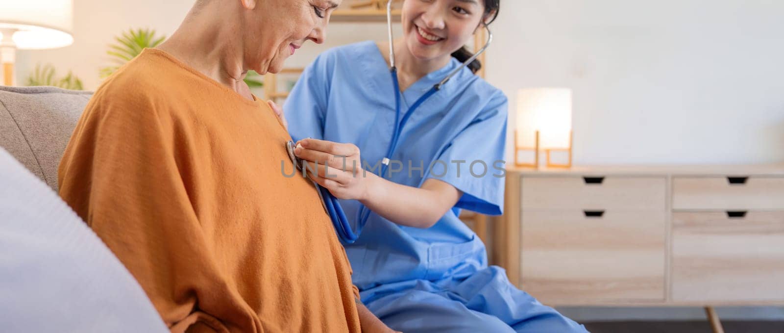 Caregiver holding stethoscope listening old patient during homecare visit. Caregiver or doctor checking heartbeat examining elderly retired woman at home. Senior heart disease, cardiology concept by nateemee