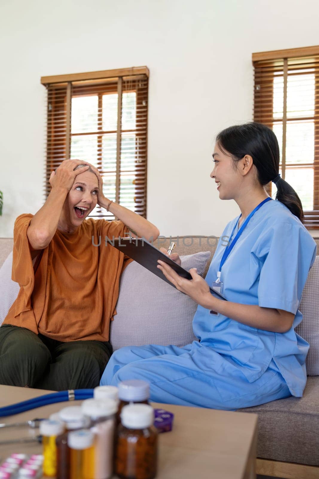 Asian young woman caregiver doctor give consultation and writing problem of elderly woman patient in room during home visit.