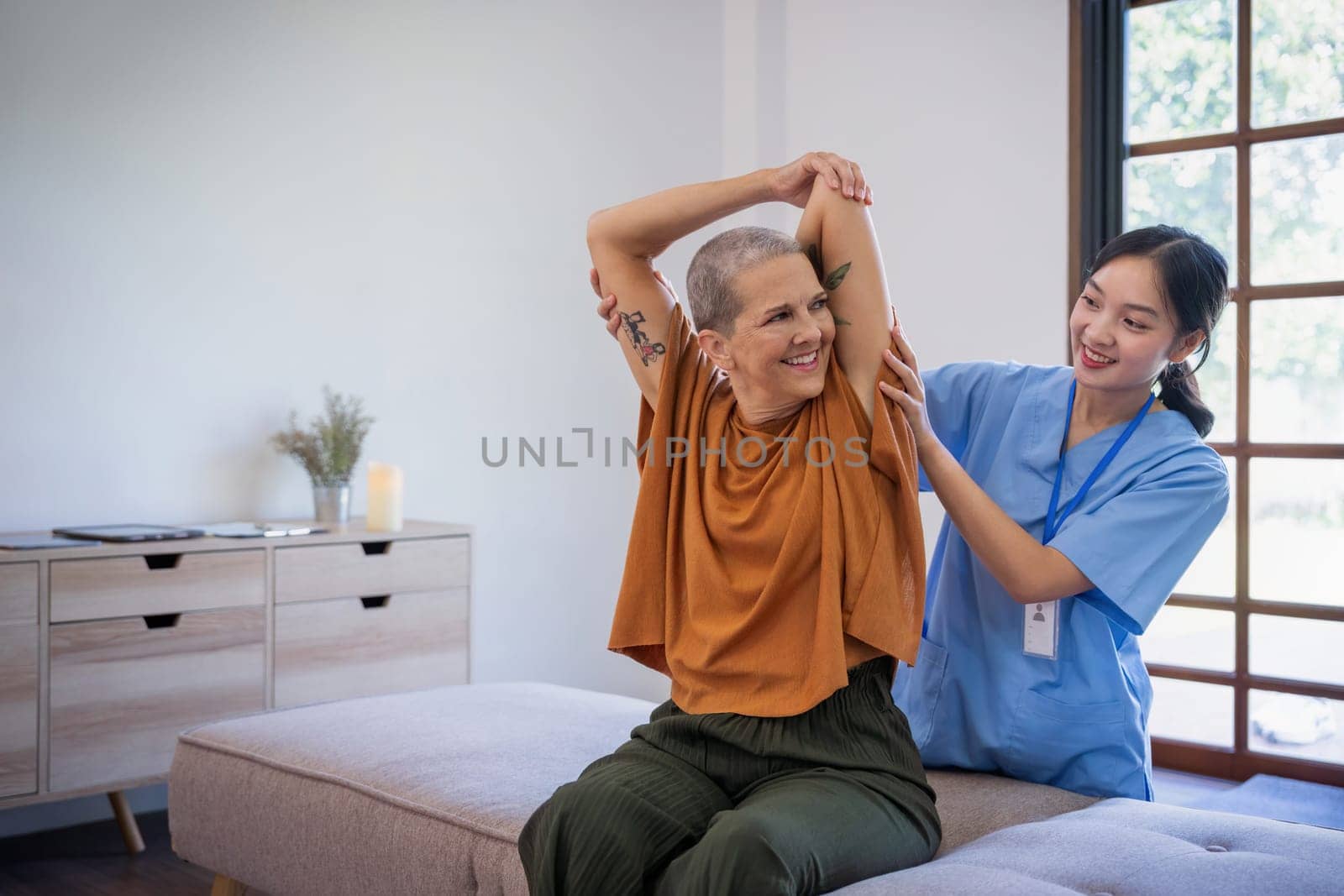 Senior elderly famale or patient sitting on sofa in living room the caregiver is checking his body in home by nateemee