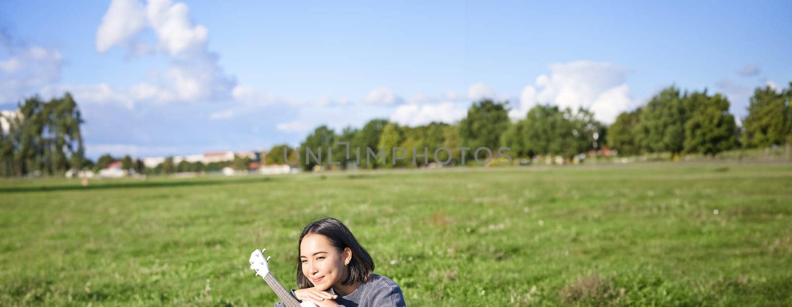 Romantic asian girl sitting with ukulele guitar in park and smiling, relaxing after university, enjoying day off on fresh air by Benzoix