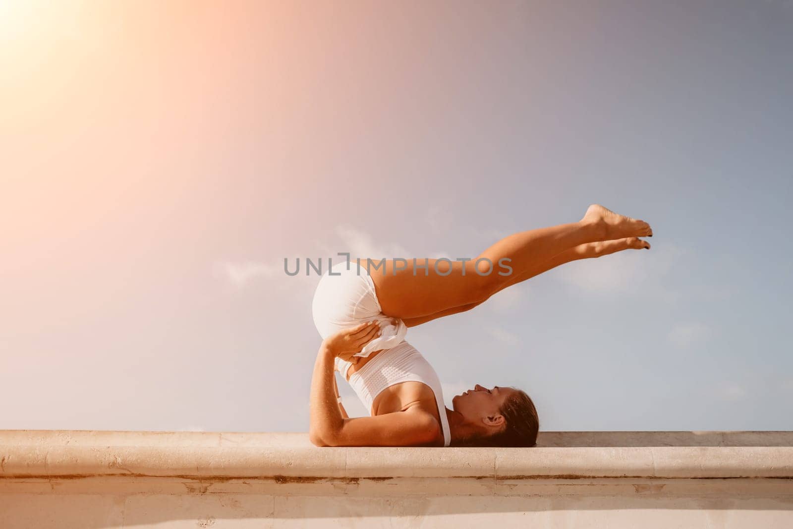 Fitness woman sea. A happy middle aged woman in white sportswear exercises morning outdoors in a park with a beach view. Female fitness pilates yoga routine concept. Healthy lifestyle. by panophotograph