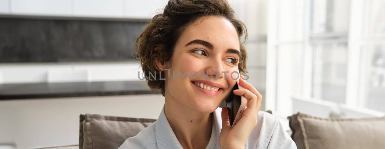 Close up portrait of smiling beautiful woman, talking on mobile phone, chats on smartphone, calls someone, sits at home.