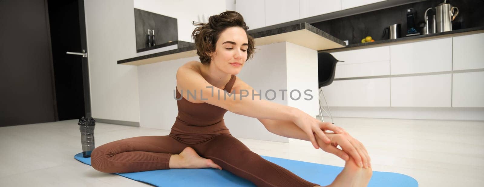 Image of brunette girl, stretching her legs, doing fitness workout, feet exercises to warm up before yoga, training at home alone.