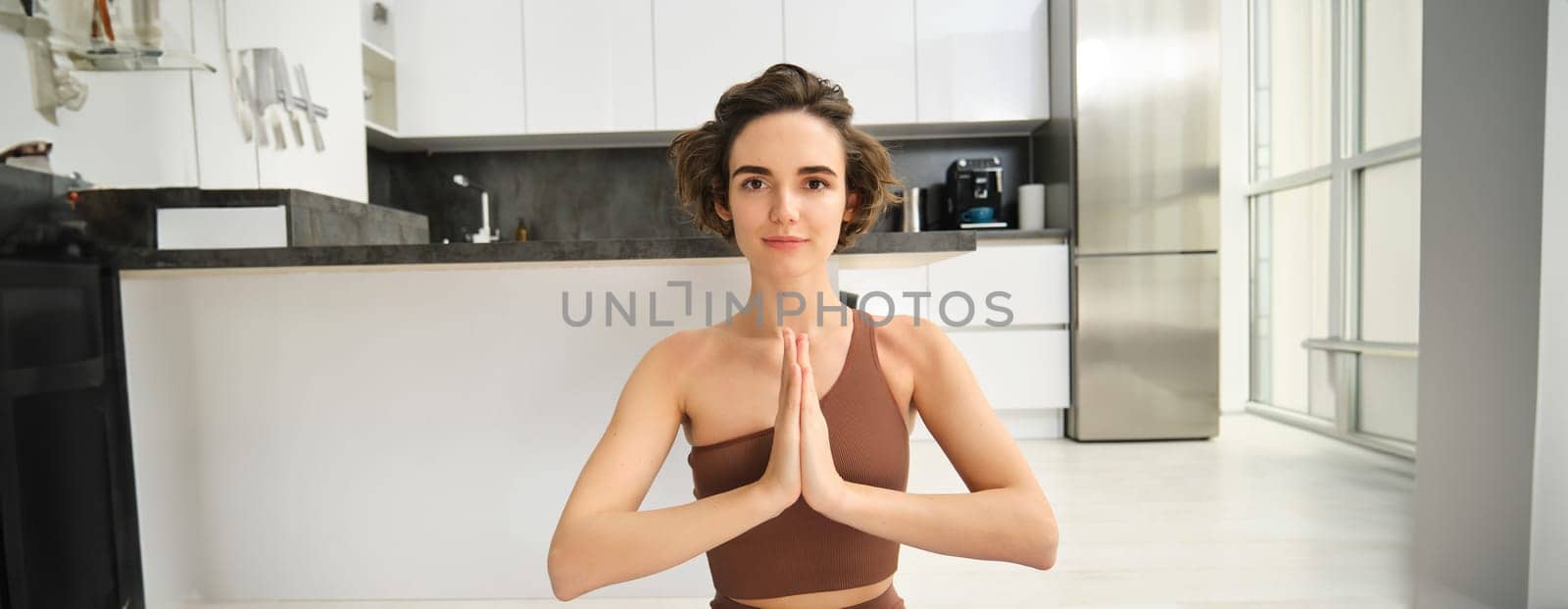 Close up portrait of young woman at home, sitting and meditating, practice yoga, making lotus pose, exercise indoors by Benzoix
