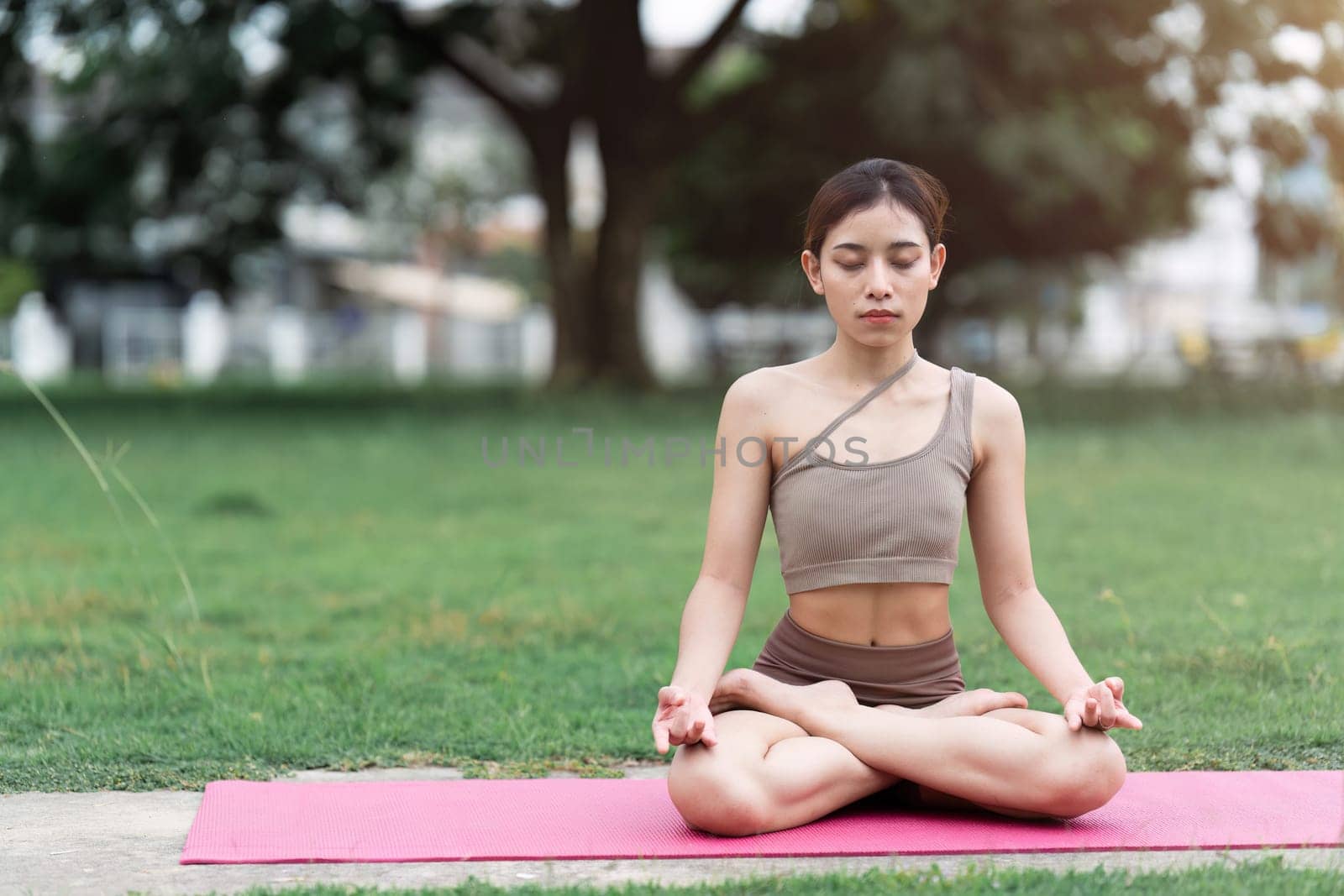 Asian woman in sporty outfit relaxing meditating feeling zen like on fitness mat in public park outdoor. Healthy active lifestyle by itchaznong
